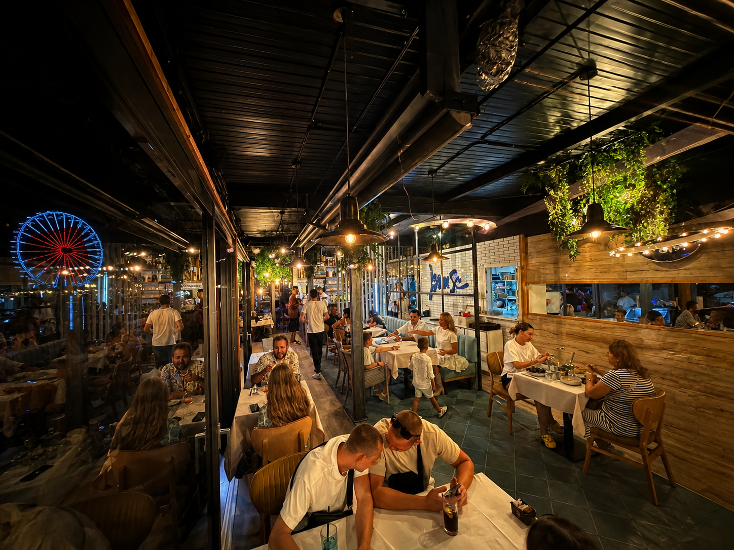 Atmosfera de seară la Muse Restaurant, terasa plină de oaspeți și roată panoramică luminată